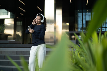 Fototapeta premium Carefree young woman dancing and listening to music on her smartphone outside a modern building.
