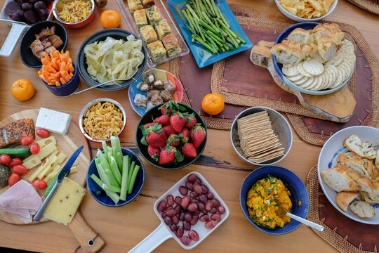 food, appetizers, party, catering, snacks, healthy, overhead shot of a large colorful spread of fresh fruits, vegetables, cheeses, and breads on a rustic wooden table for a social gathering.
