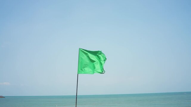 Green safety flag on sandy beach with blue sea and clear sky, safe swimming and coastal tourism.