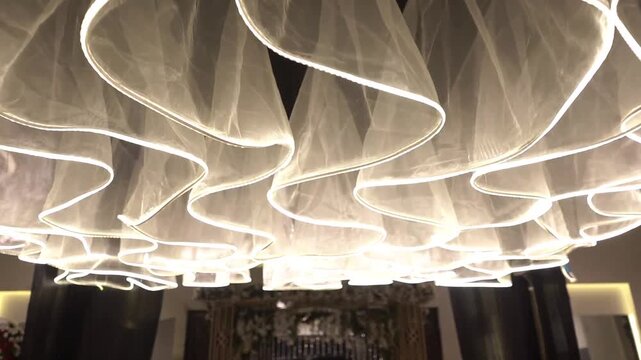 Luxury wedding hall interior featuring elegant flowing ceiling fabric installation, modern ambient lighting, and sophisticated decorative design. Ideal for wedding venues, banquet halls, event spaces,