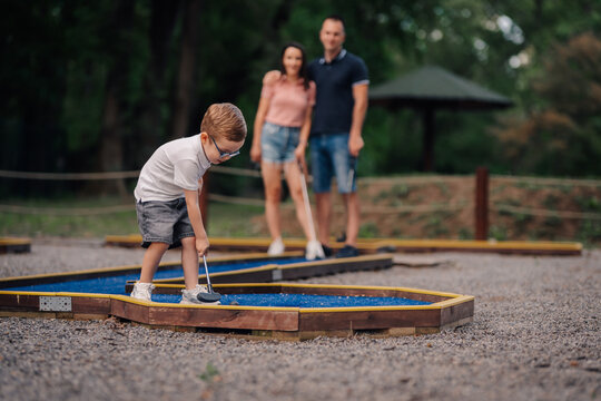 Little boy playing mini golf with parents