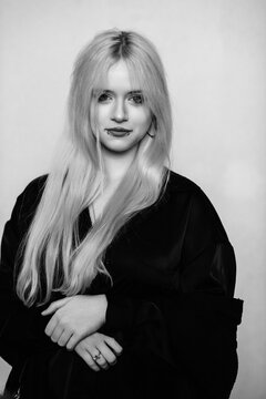 Black and white portrait of a young blonde woman with alternative style, lip piercing and a skull necklace looking away against a plain background.