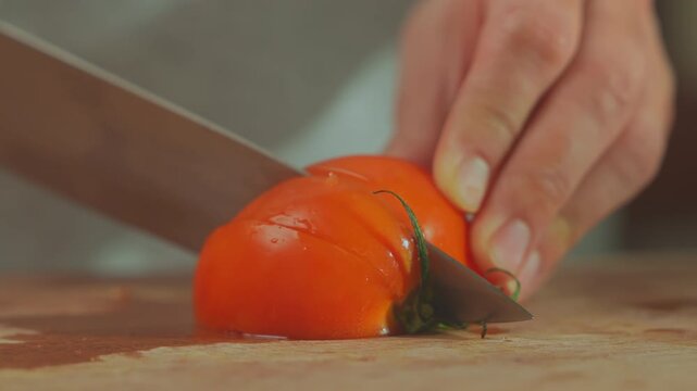 Fresh tomato being sliced with kitchen knife on wooden cutting board, healthy food preparation concept.