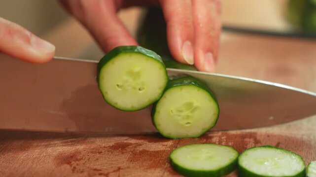 Woman hand slicing fresh cucumber with kitchen knife on wooden cutting board