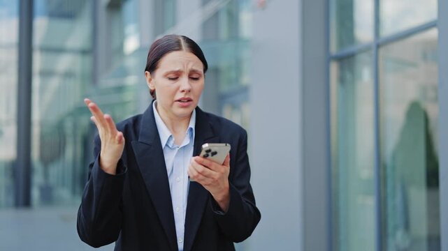 Businesswoman experiences shock and frustration reacting to distressing news on smartphone. Expresses anger, stress, and disbelief with gestures. Bad day at work leads to emotional outburst.