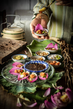 Delicious Miang Kham Bua Luan, a traditional Royal Thai appetizer featuring vibrant pink lotus petals, toasted coconut, fresh herbs, and sweet savory dipping sauce served on a wooden table.