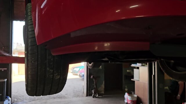 Car is lifted for repair work in garage with tools and equipment around
