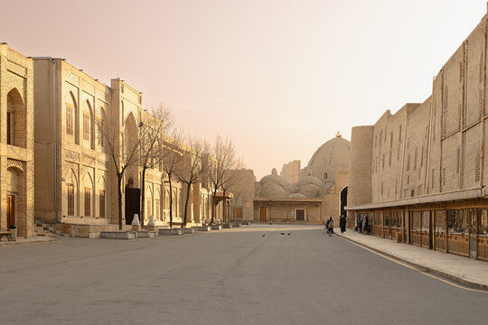 Historic street near Poi Kalyan square and Toqi Zargaron in Bukhara with monumental brick buildings and domed bazaar at dawn. Ideal for travel brochures and cultural heritage projects.