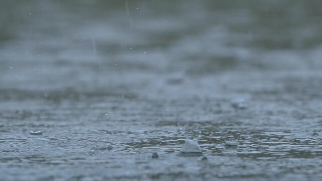 Slow motion close up of heavy rain drops falling and splashing on water surface, moody cinematic weather background.