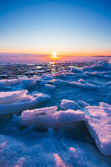 Beautiful winter landscape featuring broken ice floes, pancake ice, and snow accumulation along a freezing Nordic shoreline at sunset, captured during the golden hour in Finland. © Artem