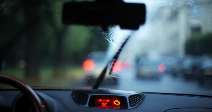 Point of view car drive in city on a rainy day with active windshield wipers and blurry bokeh street lights