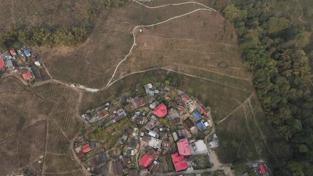 A stunning 4K drone view of a peaceful village near Mirik, Darjeeling, featuring lush farmland, green landscapes, and a winding zigzag village road surrounded by scenic Himalayan beauty.