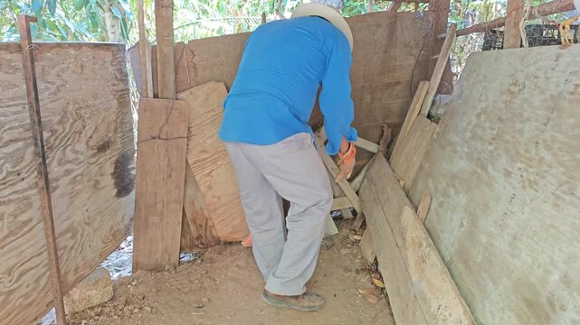 Young man organizing old wooden planks and tools inside rustic farm shed