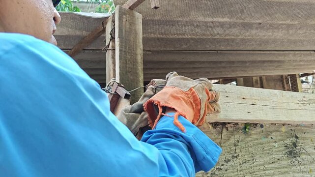Young man tying wire around metallic nail on wooden structure
