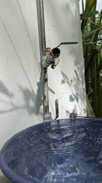 Old outdoor faucet with water leakage filling plastic bucket