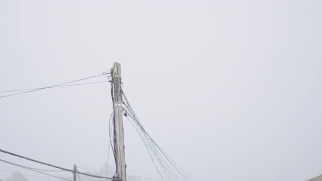Weathered utility pole and tangled wires loom against thick, stormy fog. Dramatic, muted lighting heightens the sense of isolation and tension.