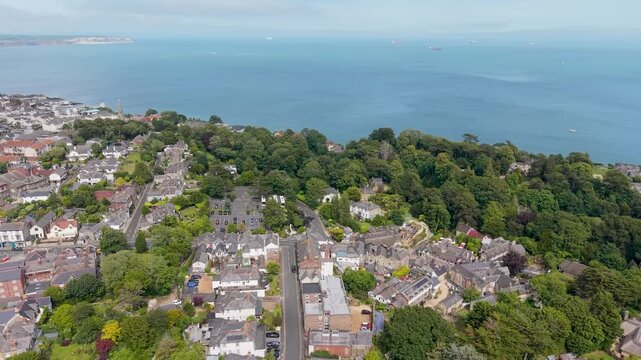 Drone view over Shanklin, Isle of Wight, moving forward across town rooftops and trees to the sandy beach, then out over the English Channel with cargo tankers on the horizon.