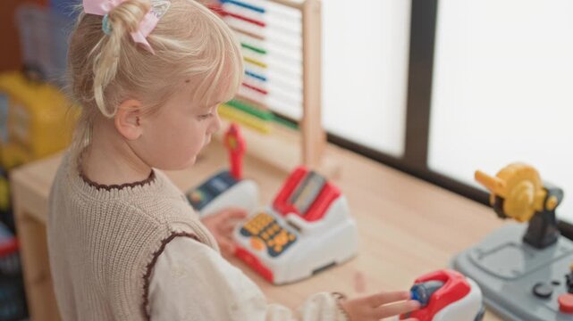 Girl pressing a toy cash register button with her hand at a wooden play counter near a window in a building; curiosity.