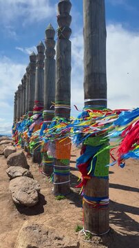 Colorful ribbons and prayer flags adorn wooden serge poles on a sunny day in Olkhonsky District, Russia