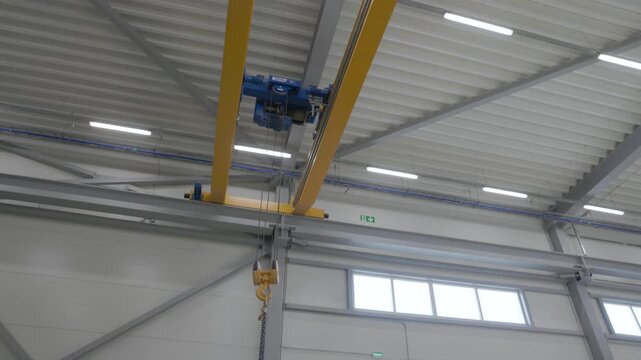 Yellow overhead crane with chain hoist mounted beneath a bright industrial ceiling in a modern factory