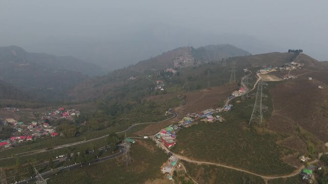 A stunning 4K drone view of a peaceful village near Mirik, Darjeeling, featuring lush farmland, green landscapes, and a winding zigzag village road surrounded by scenic Himalayan beauty.