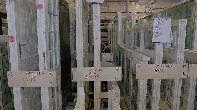 Rows of wooden doors and window frames stored upright in a factory warehouse, tagged for production and shipping