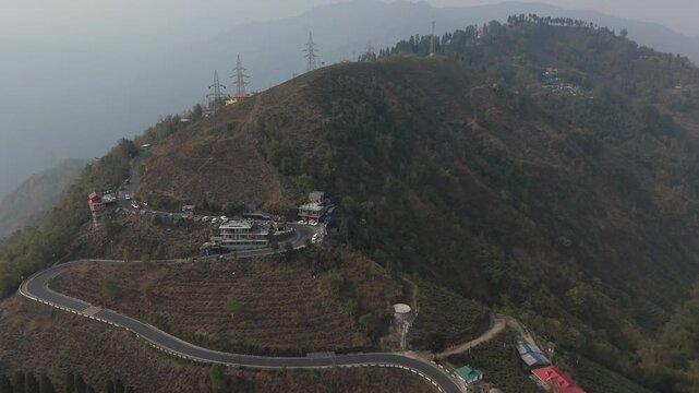 A stunning 4K drone view of a peaceful village near Mirik, Darjeeling, featuring lush farmland, green landscapes, and a winding zigzag village road surrounded by scenic Himalayan beauty.