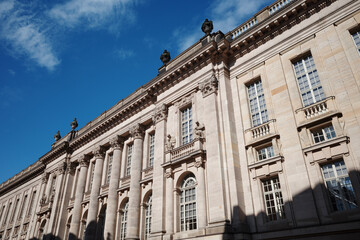 Obraz premium A low-angle view of the neoclassical facade of the historic Staatsbibliothek building on Unter den Linden in Berlin, Germany, featuring ornate stone carvings, columns, and windows.