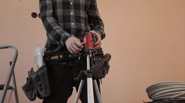 Close up of a professional turning on a laser level to mark electrical wiring layout. Preparation for precise and safe apartment electrical installation work.