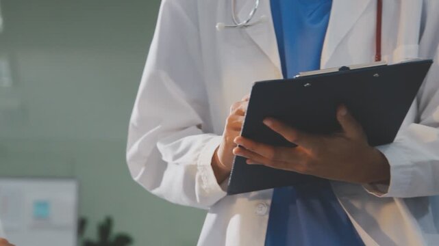 Medical professionals working together at an office desk, discussing information on a laptop, a male doctor pointing at the screen while holding a digital tablet