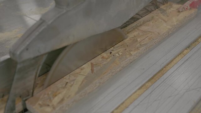 Close-up of OSB board being cut on a saw table during wood home construction, with sawdust and industrial machinery