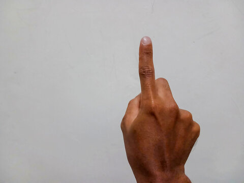 A human hand with a somewhat dark skin tone pointing its index finger straight up.