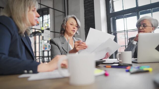 Senior ladies discussing business and finance in office, elderly woman boss. Business partners or investors examining sale reports, making decision of development in foreign markets, planning strategy