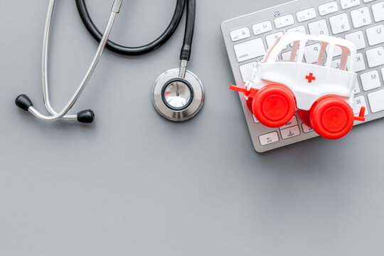 Call doctor online concept. Ambulance vehicle toy near computer keyboard and stethoscope on grey background top view space for text