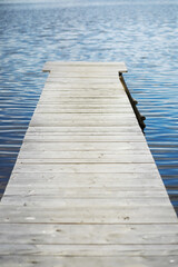 Fototapeta premium Serene Wooden Dock Extending Into Calm Blue Lake Waters on a Sunny Day
