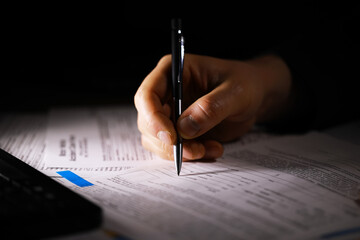 Hand Writing on Documents with Pen in Dim Lighting - Business, Work, and Paperwork Concepts © alexkich