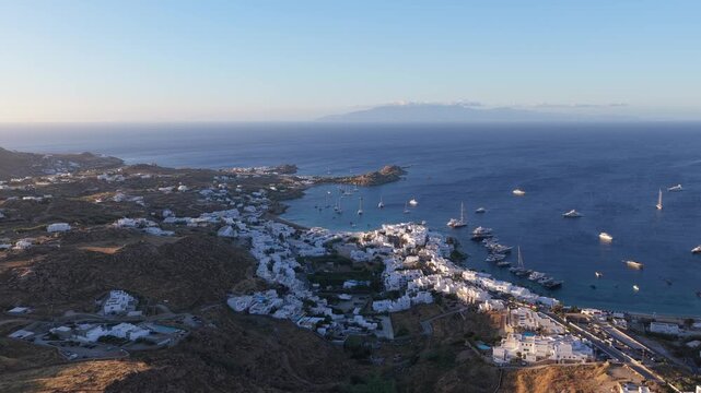 Scenic aerial of Mykonos coastline with white buildings, Aegean Sea, distant greek islands, luxury yachts moored during summer holiday