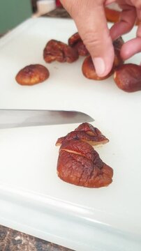 A person using a kitchen knife to slice fresh shiitake mushrooms on a white cutting board for meal preparation