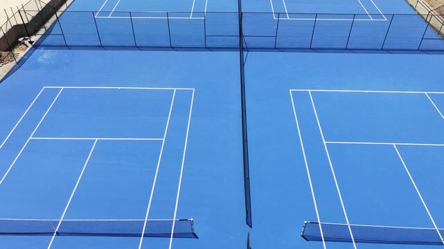 Sweeping drone aerial perspective gliding over a complex of perfectly manicured blue tennis courts, geometric, view