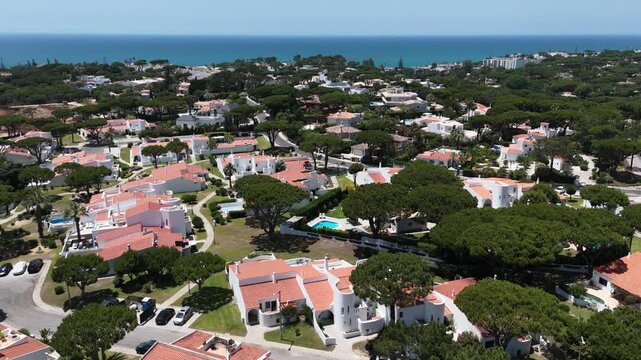 Aerial overview of Quinta do Lago resort buildings in Vale de Lobo, Algarve, Portugal, Europe. Shot of rooftops of luxury cottages in green landscape with mountains on background. Golf fields.