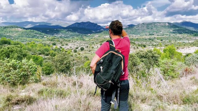 Male hiker with backpack looking at green mountain valley view during summer trekking
