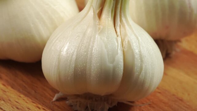 Single garlic bulb with peeled skin slowly rotating on wooden background,close up, macro.