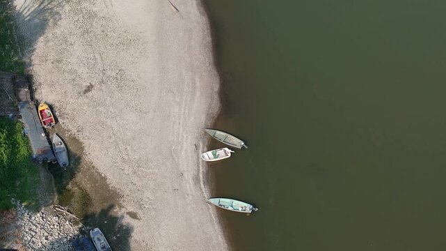 Small boats rest on an exposed gravel shoreline of the Po River near Cremona, Lombardy, Italy, as severe summer drought lowers water levels and reveals extensive sediments across Po Valley, top down
