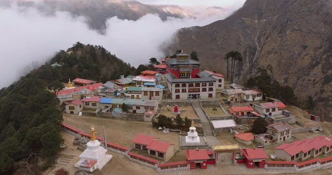 Tengboche, Everest Region, Nepal, drone orbit shot of the historic Tengboche Monastery complex situated on a hill surrounded by pine forests and misty mountain clouds.
