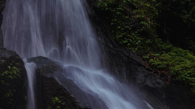Slow shutter speed shot of a Bali waterfall near Ulu Petanu waterfall, Indonesia. Cinematic. Green vegetation and rocks.