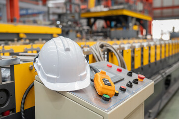 Fototapeta premium White safety helmet and handheld control unit rest on industrial control panel in bright metal fabrication plant, conveying safety focus and organized production workflow with warm tones and depth