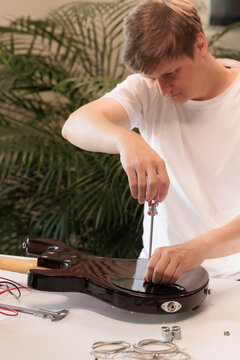 Young repairman opening a bass guitar control cavity with a screwdriver