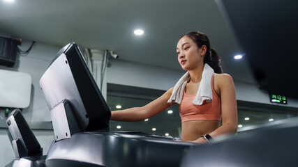 Fototapeta premium Asian woman running on treadmill for cardio workout in gym