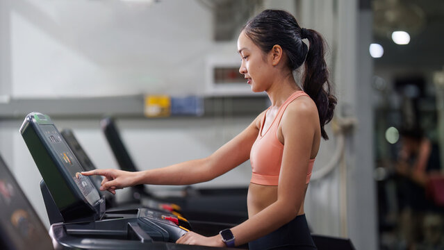 Asian woman using treadmill console screen in gym for cardio workout