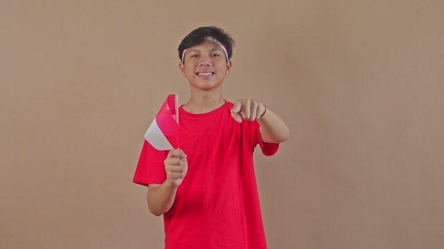 Happy Indonesian teen holding mini flag and pointing forward at camera